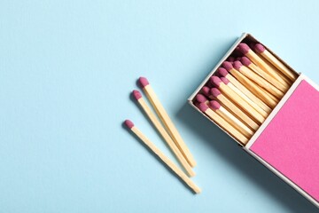 Matches and box on light blue background, flat lay. Space for text