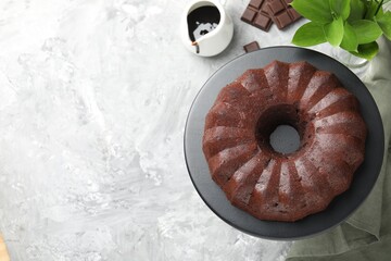 Tasty bundt cake, pieces of chocolate, sauce and green leaves on grey table, flat lay. Space for text