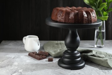 Tasty bundt cake, pieces of chocolate, sauce and green leaves on grey table