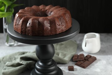Tasty bundt cake, pieces of chocolate, sauce and green leaves on grey table, closeup