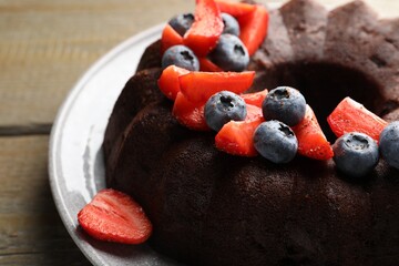 Tasty chocolate bundt cake with berries on wooden table, closeup