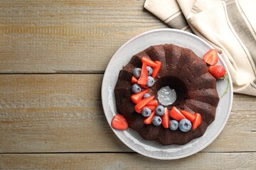 Tasty chocolate bundt cake with berries on wooden table, top view. Space for text