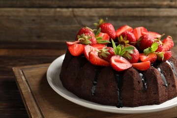 Delicious chocolate bundt cake with strawberries and mint on wooden table, closeup