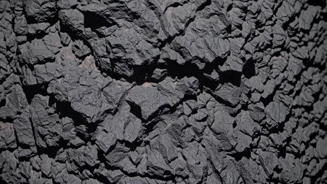 Weathered dark gray volcanic rock displaying intricate, rugged mineral texture, highlighting geological surface through detailed close-up perspective