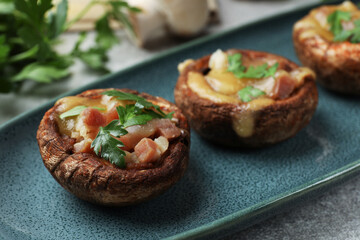 Delicious stuffed mushrooms with melted cheese and parsley on grey textured table, closeup