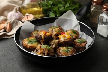Tasty stuffed mushrooms in frying pan and ingredients on black table, closeup