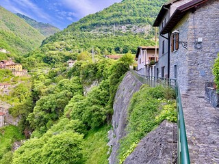 Hillside village in Lenno Ossuccio, with colorful houses, winding stone alleys, lush greenery, steep cliffs and panoramic view of church tower above the forested valley