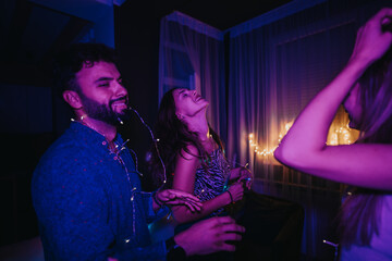A group of happy friends enjoying and dancing during a nighttime celebration, indoors with colorful lights. The atmosphere complements the cheerful and spirited vibe of the evening gathering.