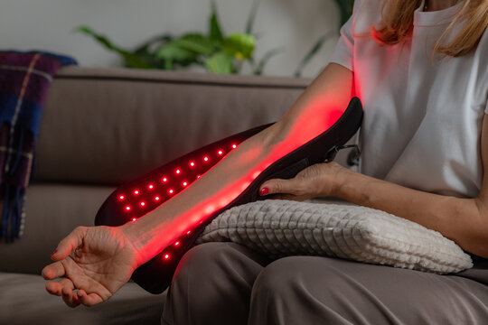 Red light therapy pad used at home relieves a womans elbow pain from strain or injury. It boosts blood flow and aids tissue healing, enhancing comfort and mobility with non-invasive care