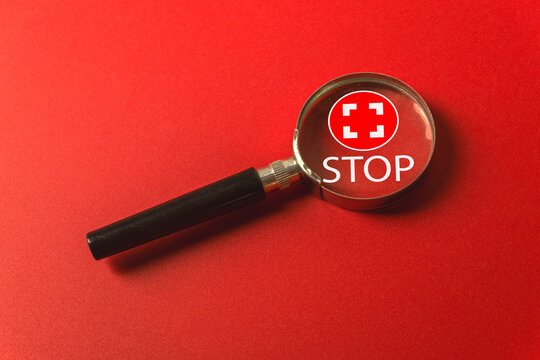 Magnifying glass focusing on a red circular icon with 'STOP' text and focus frame symbol. Concept of analyzing a stop command, halting an activity, safety instruction, or reaching a defined limit.