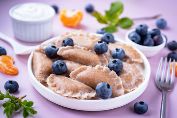 Healthy breakfast: diet dumplings with cottage cheese and berries on a white plate on a pink background. Whole wheat flour dumplings with berries.
