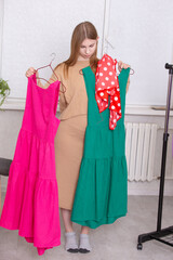 Choosing between a pink and a green dress while preparing for an event in a bright room