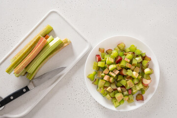 Freshly chopped green rhubarb in white plate on white background. Trendy organic food. Ready for...