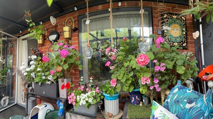 Landscape of a pretty balcony full of colourful Geranium Flowers and hanging garden decor, which is reflected in the window behind
