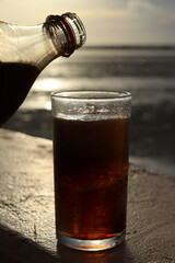 Pouring cola drink on glass with ice cubes