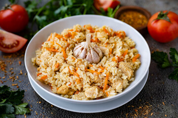 Dinner dish: hearty pilaf with chicken in a white plate on a gray background. Home cooking. Rice with chicken for lunch. Close-up