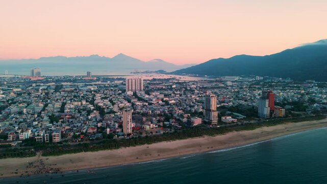Aerial view capturing da nang's modern skyline blending with the tranquil coastline of son tra peninsula, illuminated by the warm hues of a vibrant sunset