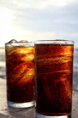 Cola drink with ice cubes and beach with blue sky