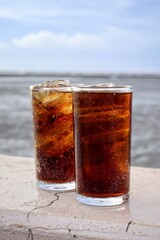 Cola drink with ice cubes and beach with blue sky