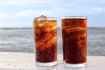 Cola drink with ice cubes and beach with blue sky