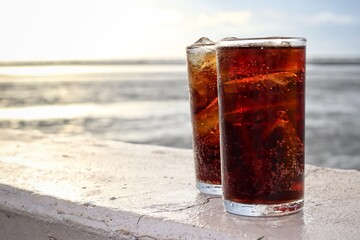 Cola drink with ice cubes and beach with blue sky