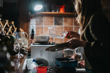 A young woman washing dishes in a warmly lit home kitchen setting during the evening.
