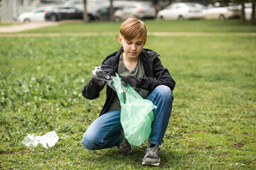 Teenager kid boy picking up trash plastic bottles in the park. Volunteer concept. Ecology,...