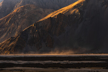 Golden sunlight casts long shadows across the dramatic Nubra Valley landscape, revealing rugged...
