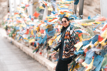 Woman traveler explores Leh Ladakh, India, walking beside colorful Tibetan prayer flags, embracing Himalayan culture, spiritual atmosphere on adventurous mountain journey