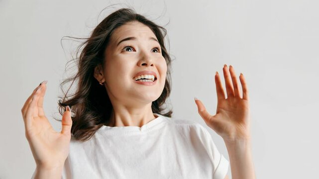 Wow. Beautiful female portrait against gray studio background. Young emotional surprised Asian woman standing with open mouth. Animated clip. Human emotions, facial expression concept