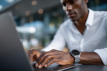 A close-up of a man intently using his laptop while wearing a stylish watch, capturing the essence of modern professionalism and technology use in a contemporary workspace.