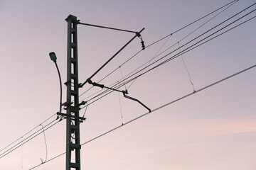 Overhead line equipment (OLE) used for railway electrification with catenary system and supporting pole. Infrastructure for trains against pastel evening sky, arrangement of wires and insulators