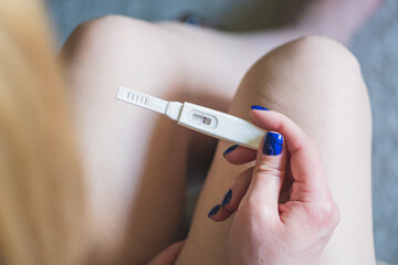 Young blonde girl sitting and looking at a negative pregnancy test, top view