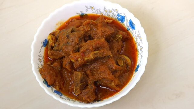 Delicious mutton curry in white bowl on light wooden table. Spicy, popular Bengali mutton bhuna.