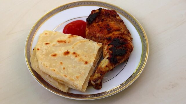Grilled barbecue chicken with Paratha and tomato sauce on ceramic plate, wooden surface. Delicious, healthy meal.