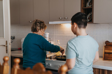 An elderly woman prepares food on the stove while a young boy watches her in a well-lit, modern...