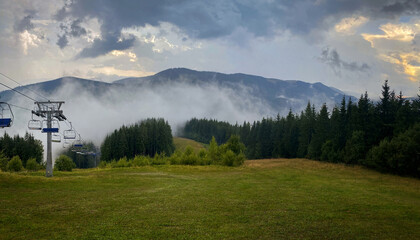 Cableway in the Carpathian mountains. The sun comes out from behind the storm clouds after the rain. A thick fog rolls over the forest and mountains.