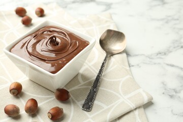 Tasty chocolate spread and hazelnuts on table, closeup