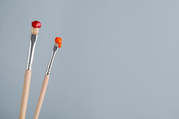 Two brushes with color paints on light grey background, closeup. Space for text