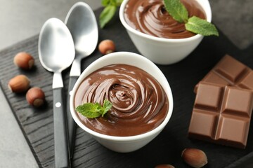 Tasty chocolate spread, pieces, mint and hazelnuts on table, closeup