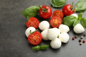 Mozzarella cheese, tomatoes, basil and peppercorns on grey table, closeup