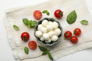Tasty mozzarella cheese balls, tomatoes and basil on white wooden table, flat lay