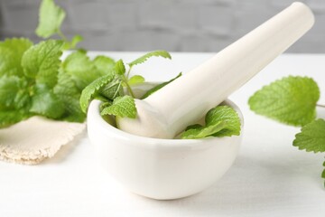 Fresh lemon balm leaves and pestle in mortar on white wooden table, closeup