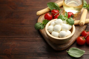 Tasty mozzarella cheese balls, breadsticks, tomatoes and basil on wooden table. Space for text