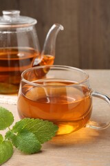Aromatic lemon balm tea in glass cup, teapot and fresh leaves on wooden table, closeup