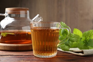 Aromatic lemon balm tea in glass cup, teapot and fresh leaves on wooden table