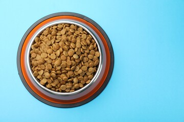 Dry pet food in feeding bowl on light blue background, top view. Space for text