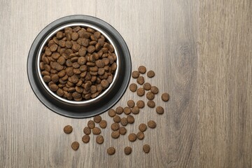 Dry pet food in feeding bowl on wooden background, top view. Space for text
