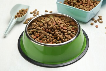 Dry pet food in feeding bowl, container and scoop on light background, closeup