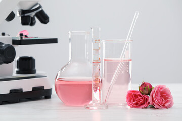 Making luxury perfume. Essential oils in glassware, flowers and microscope on white wooden table,...